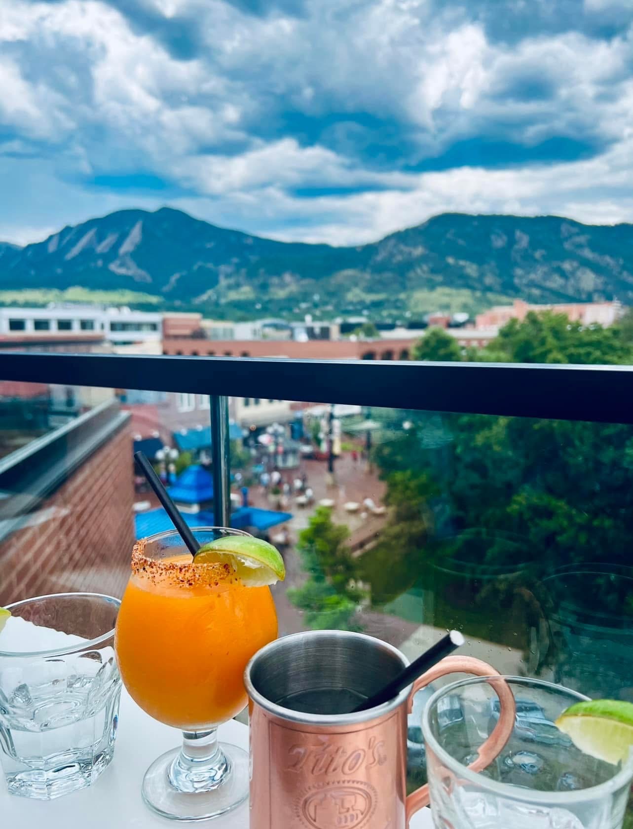 Spicy orange cocktail and a copper mule mug on a rooftop with mountains behind