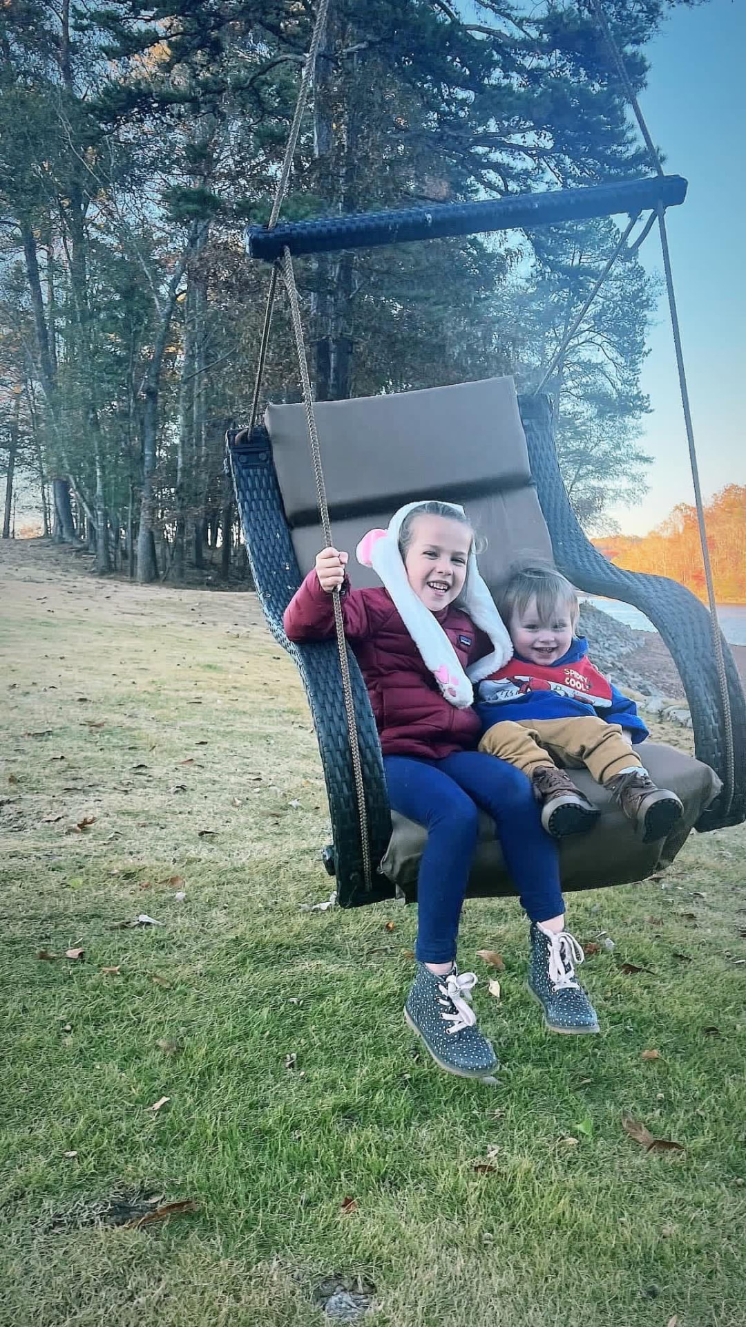 Two young kids smiling together on a hanging swing chair at sunset